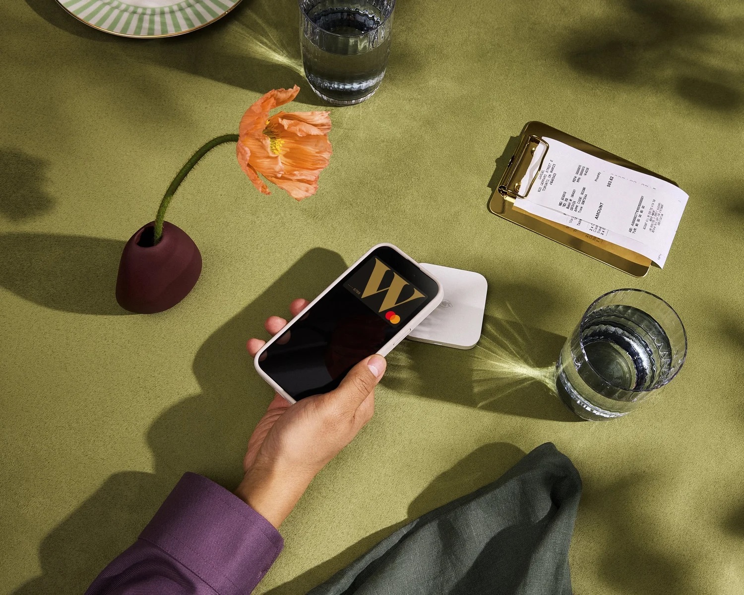 Hand holding smartphone above green tabletop with drink and styled lifestyle objects