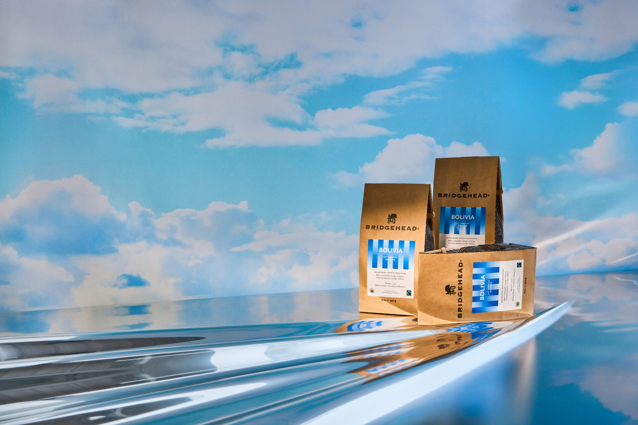 Coffee packaging on a reflective surface with blue sky backdrop, clean commercial product shot