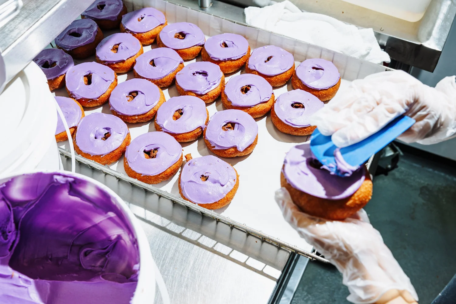 Rows of purple-frosted donuts on cooling rack, bakery production scene