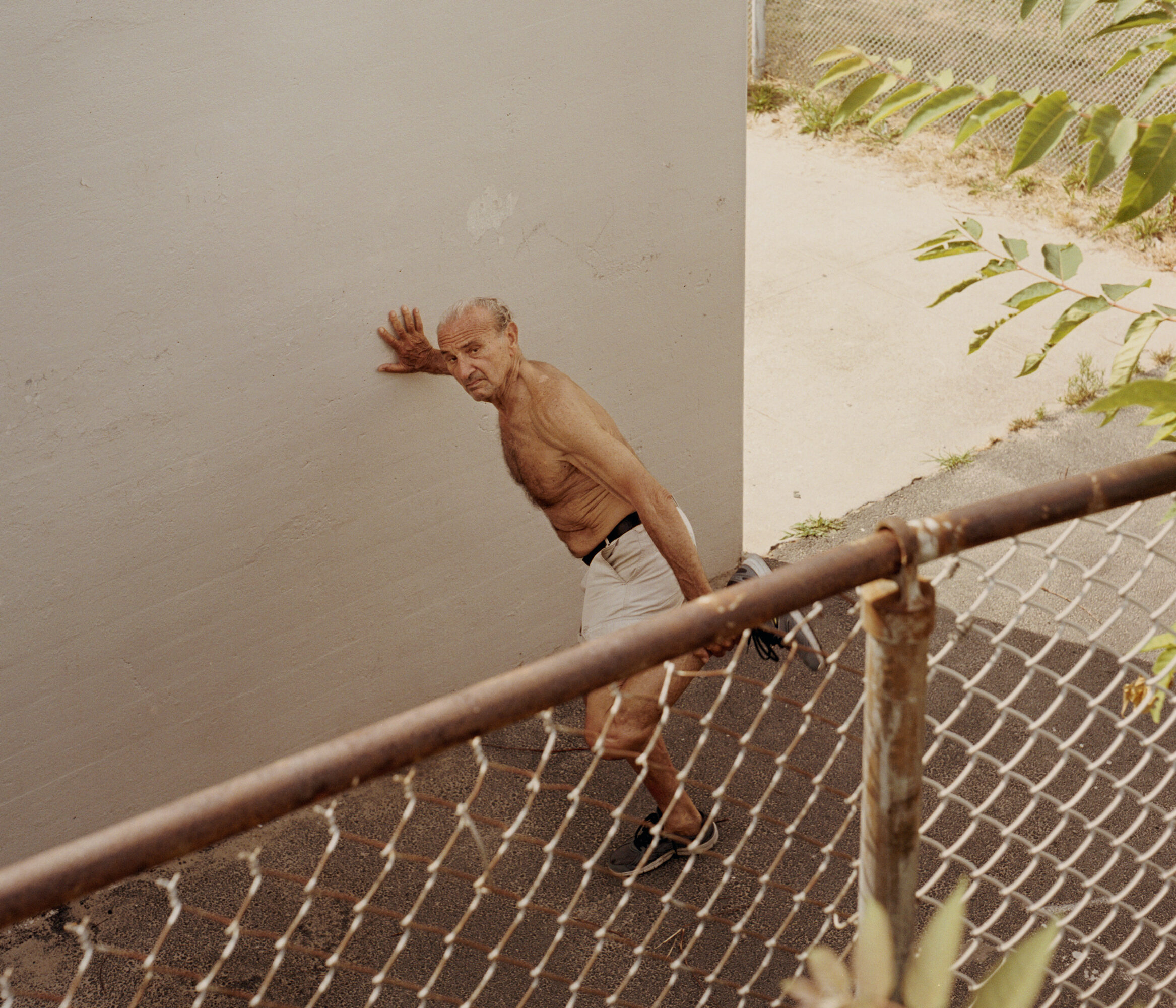 Tightrope walker balancing beside a chain-link fence outdoors