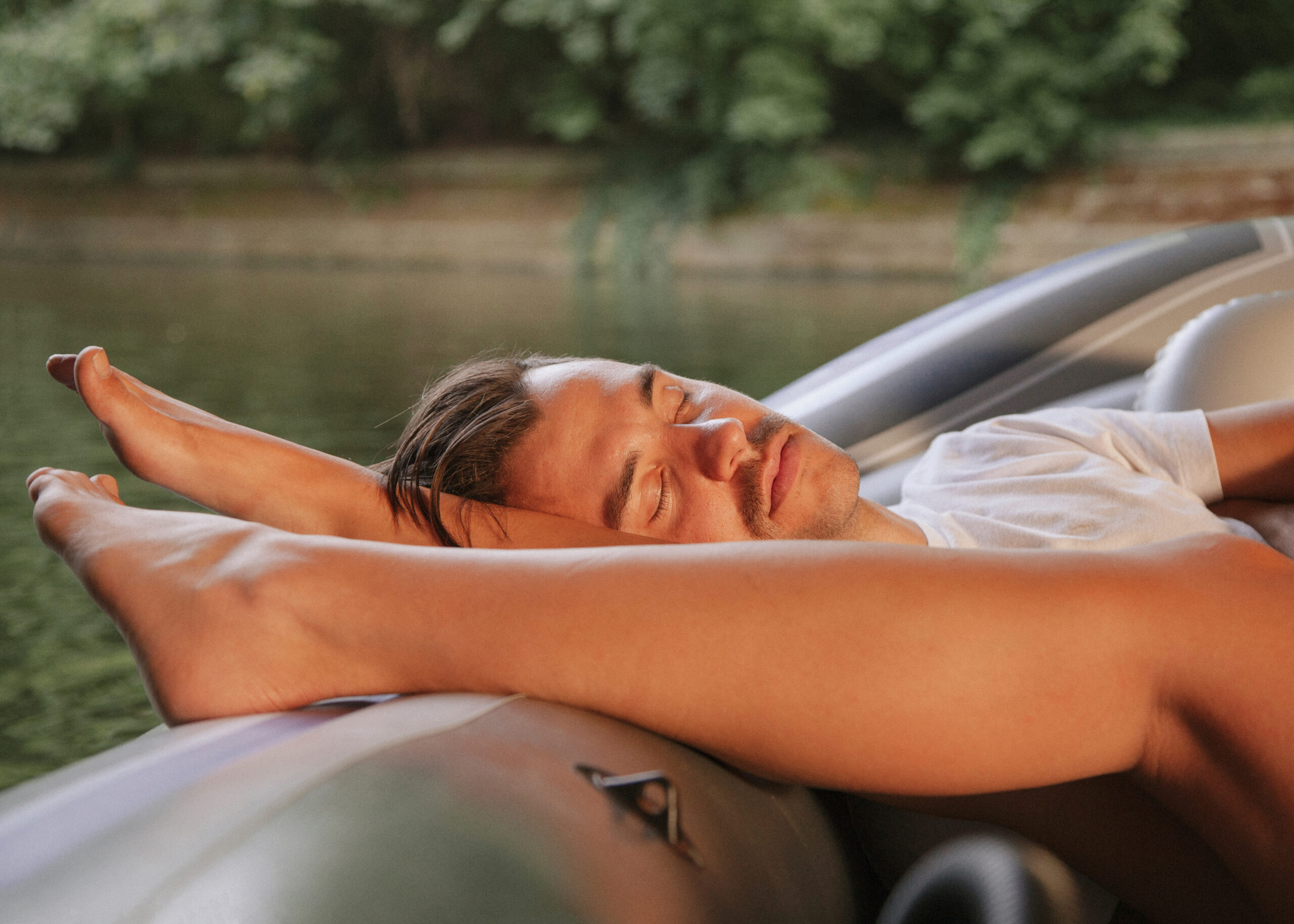 Person reclining with arms behind head near a reflective surface outdoors