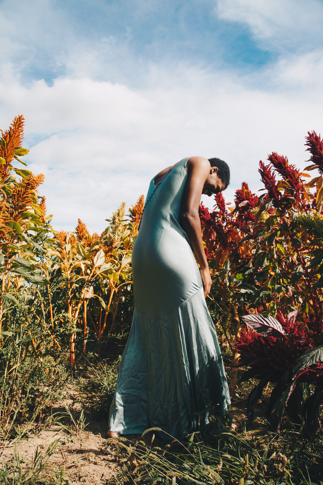 Person in a blue dress bending forward among colorful plants, fashion portrait outdoors