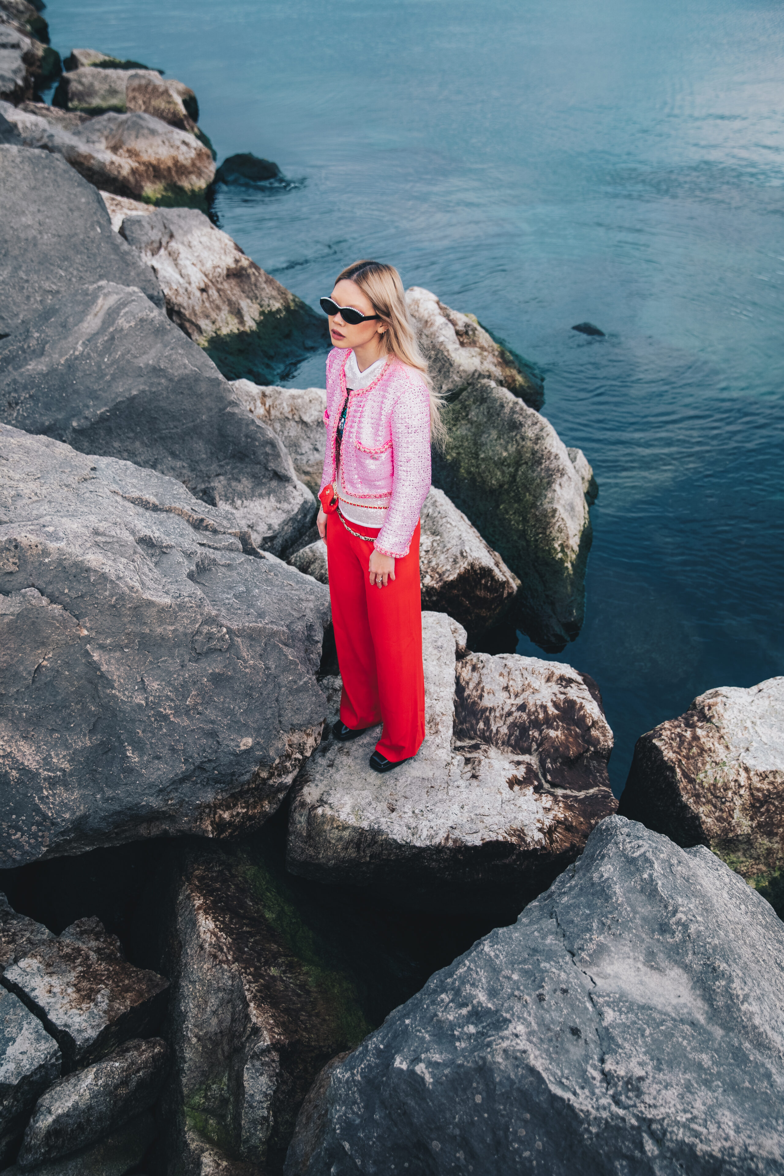 Woman in bright pink outfit standing on rocks by the water, lifestyle fashion photography