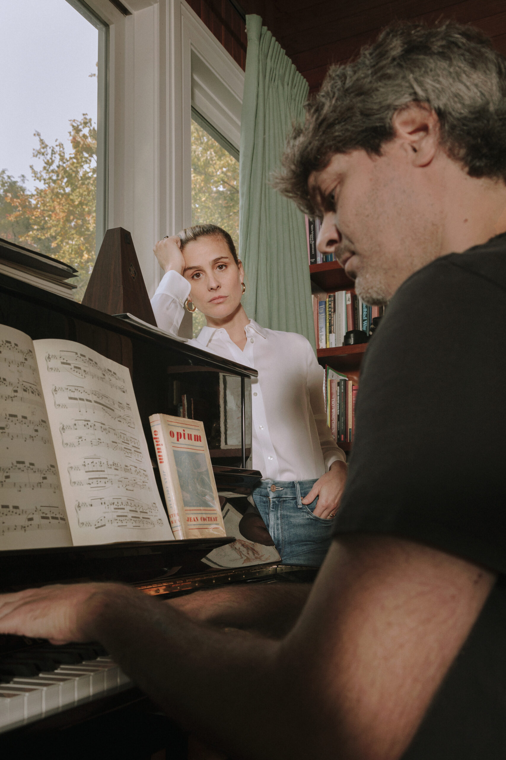 Two people in a room looking at music papers with a piano