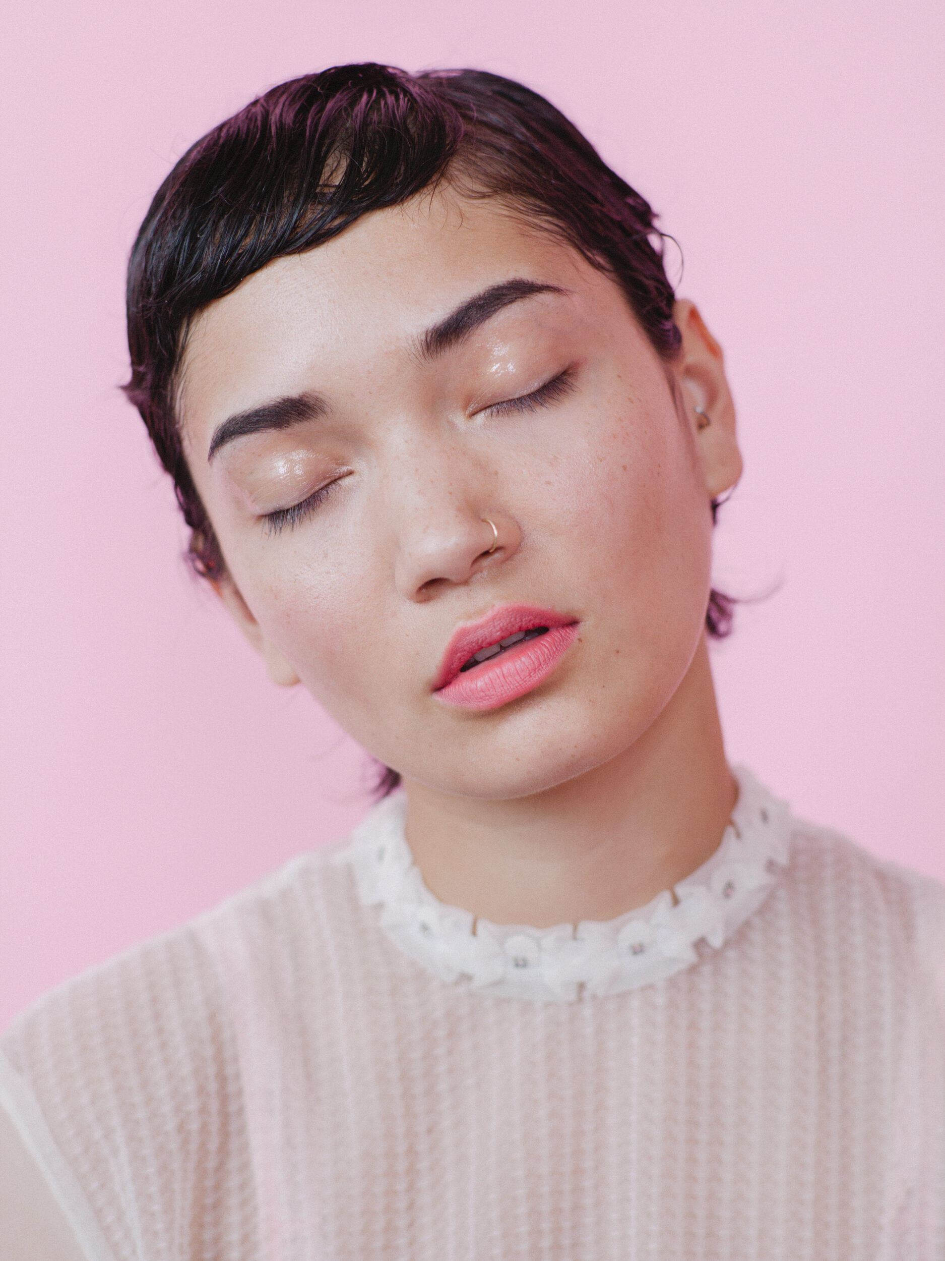 Beauty portrait of a person with eyes closed on a pink background, soft light and smooth styling.