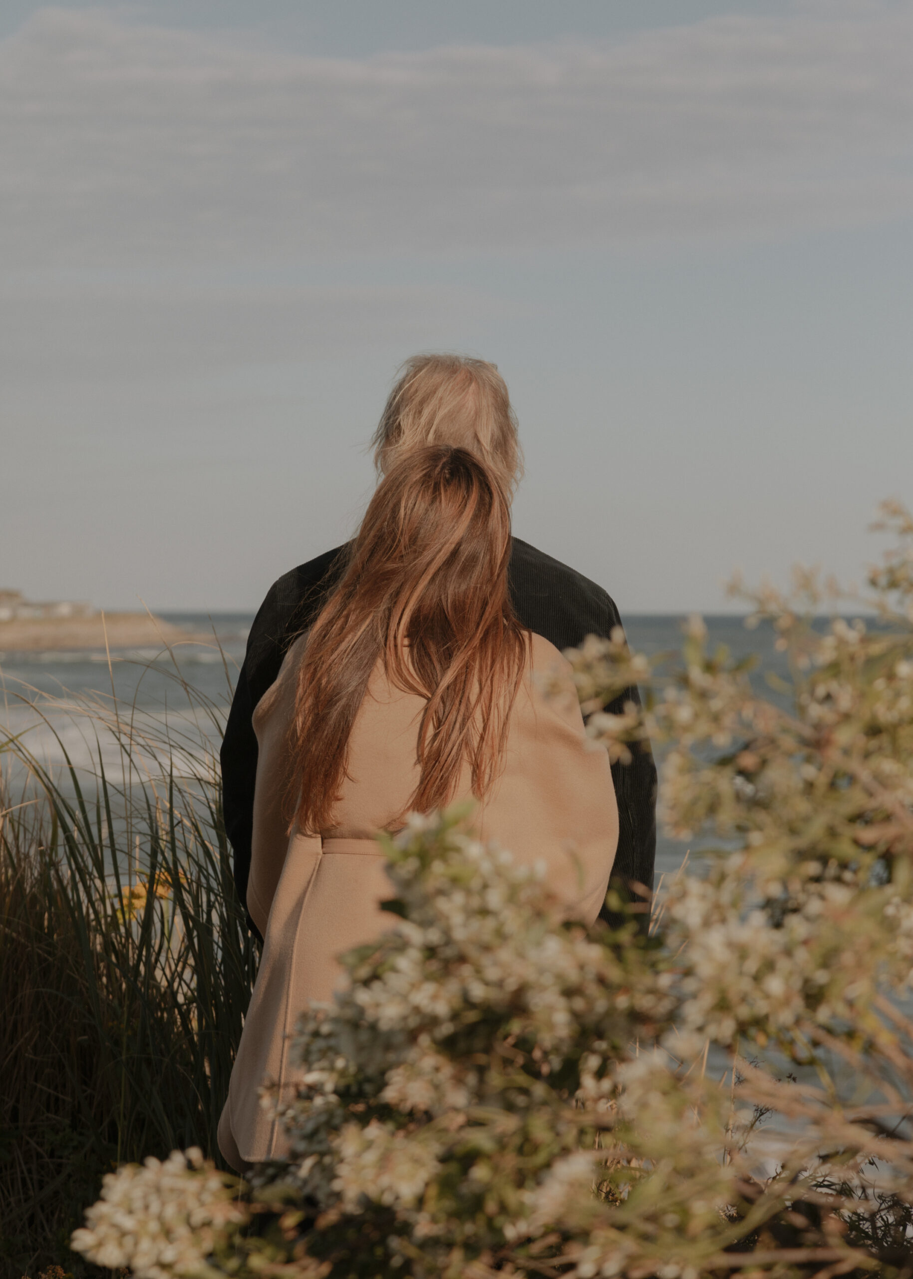 Person walking through tall grass or dunes, photographed from behind in natural light.