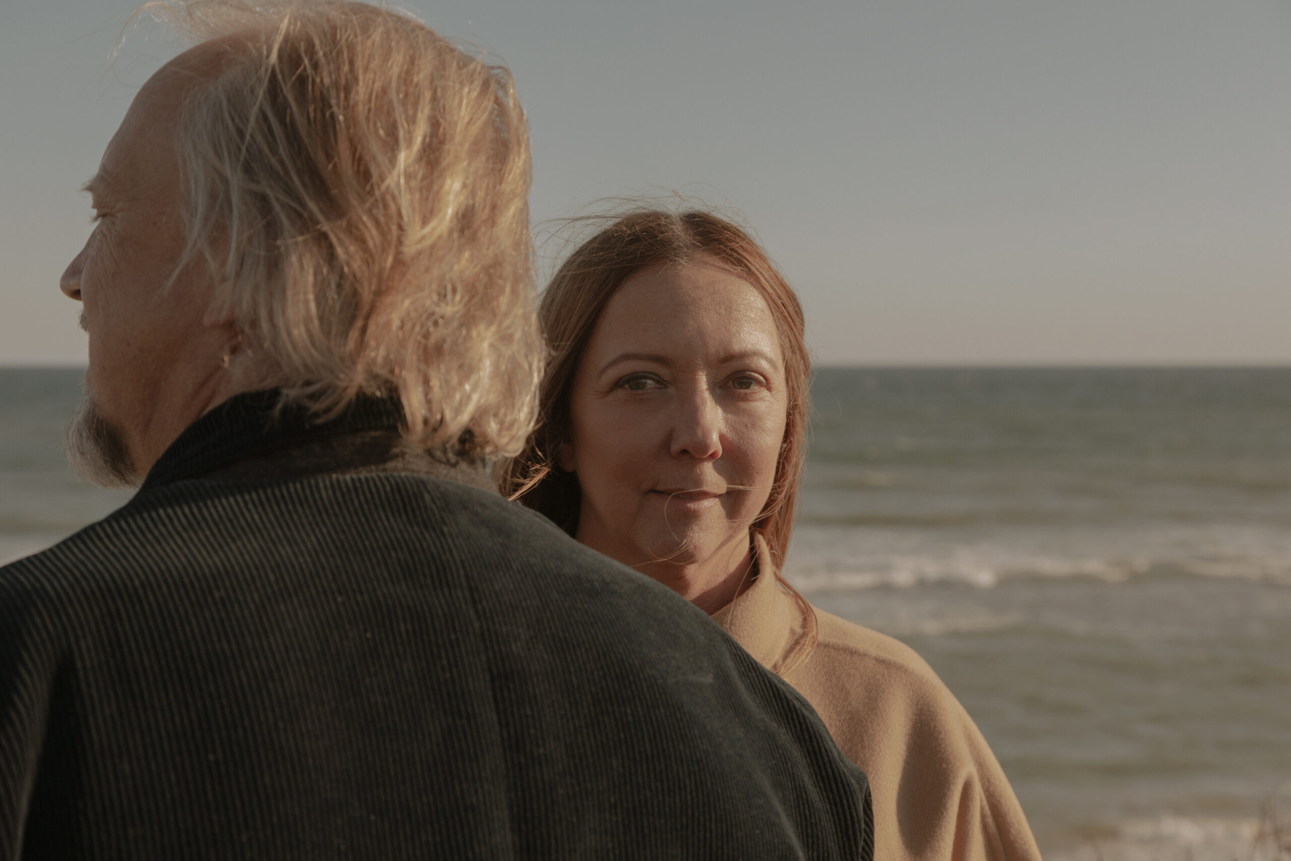 Two people outdoors near the ocean, candid moment with soft coastal light.