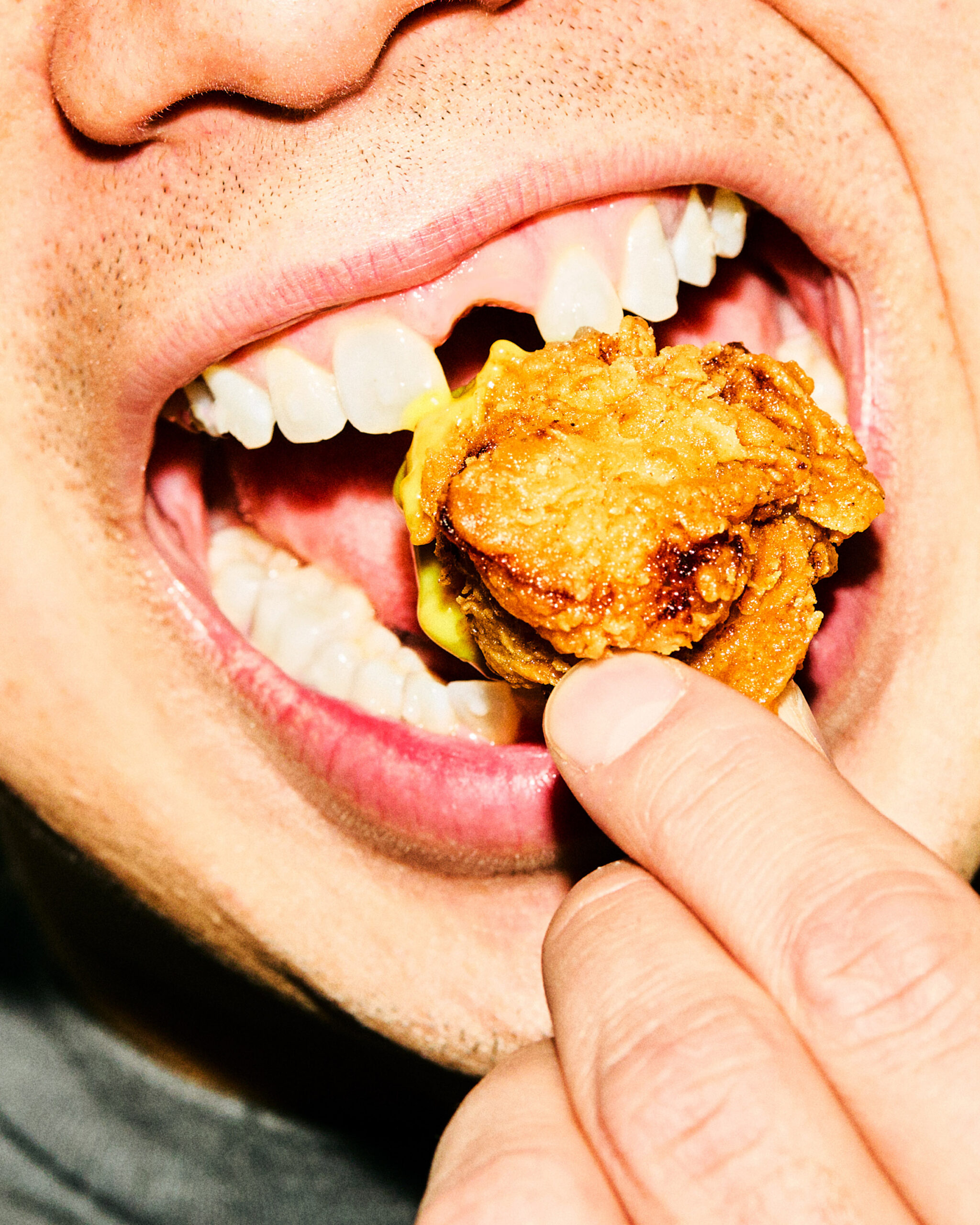 Close-up of a mouth biting into a piece of fried chicken