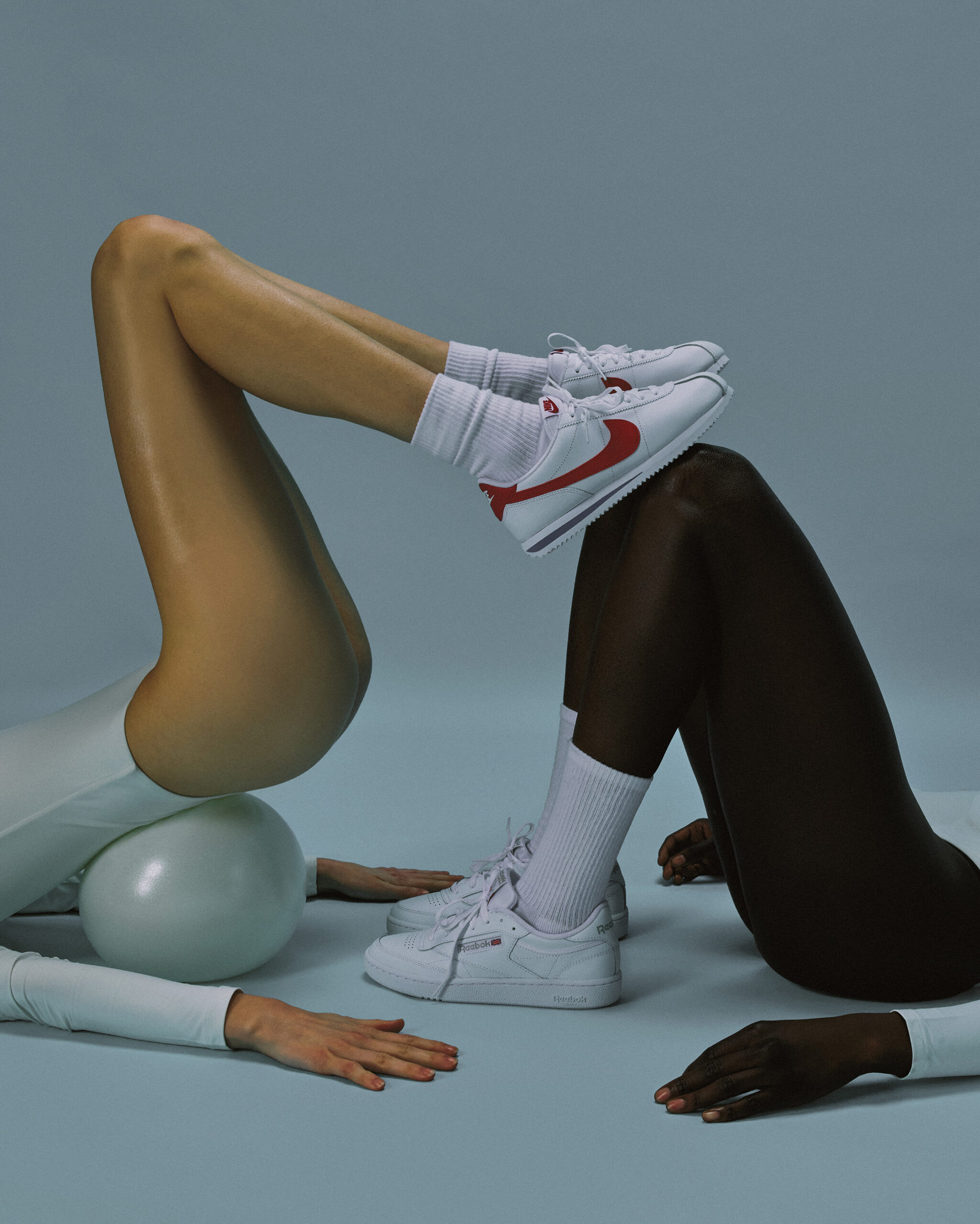 Athletic fashion pose with bent legs, white sneakers, and sculptural exercise balls