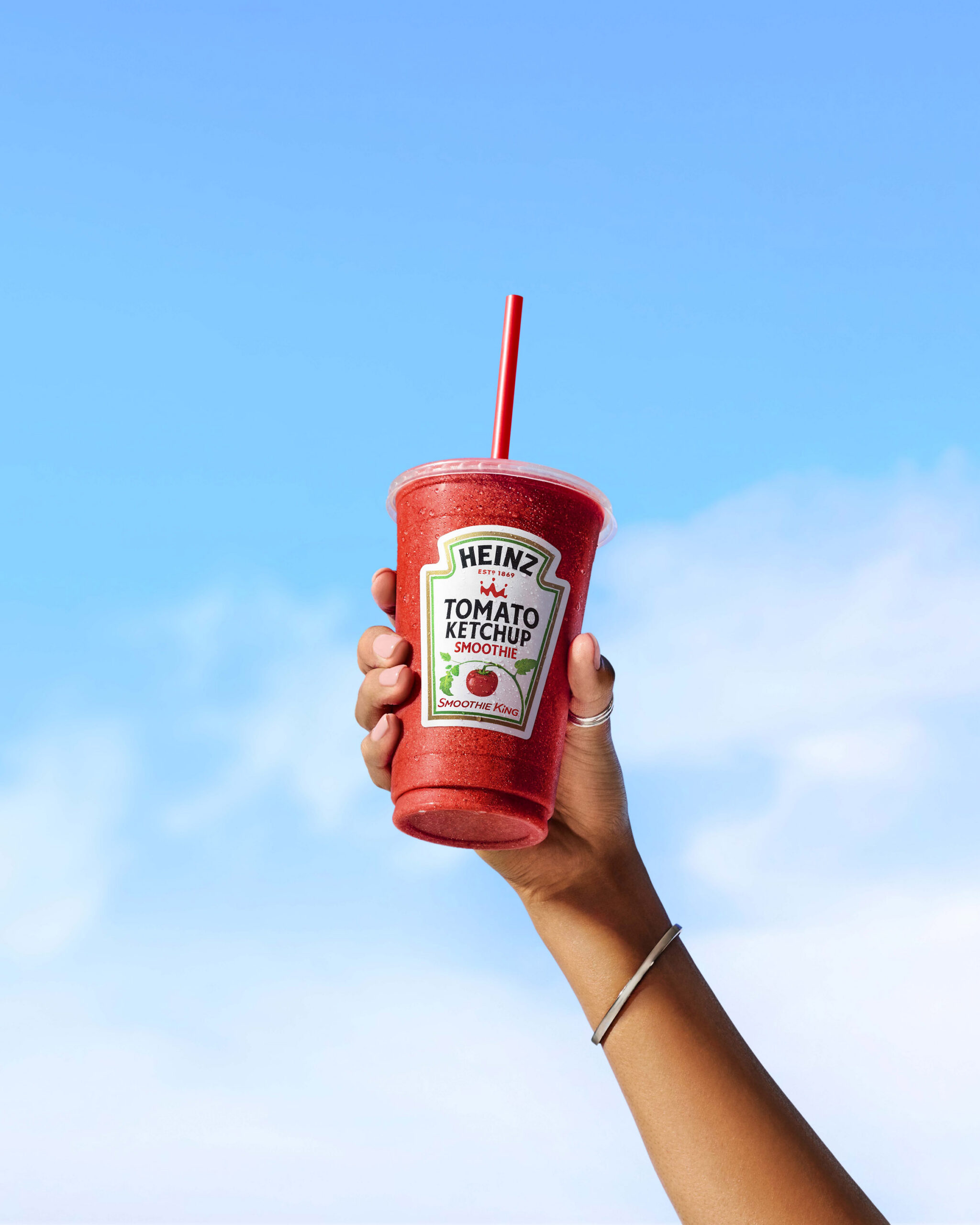 Hand holding a red ketchup cup against a bright blue sky
