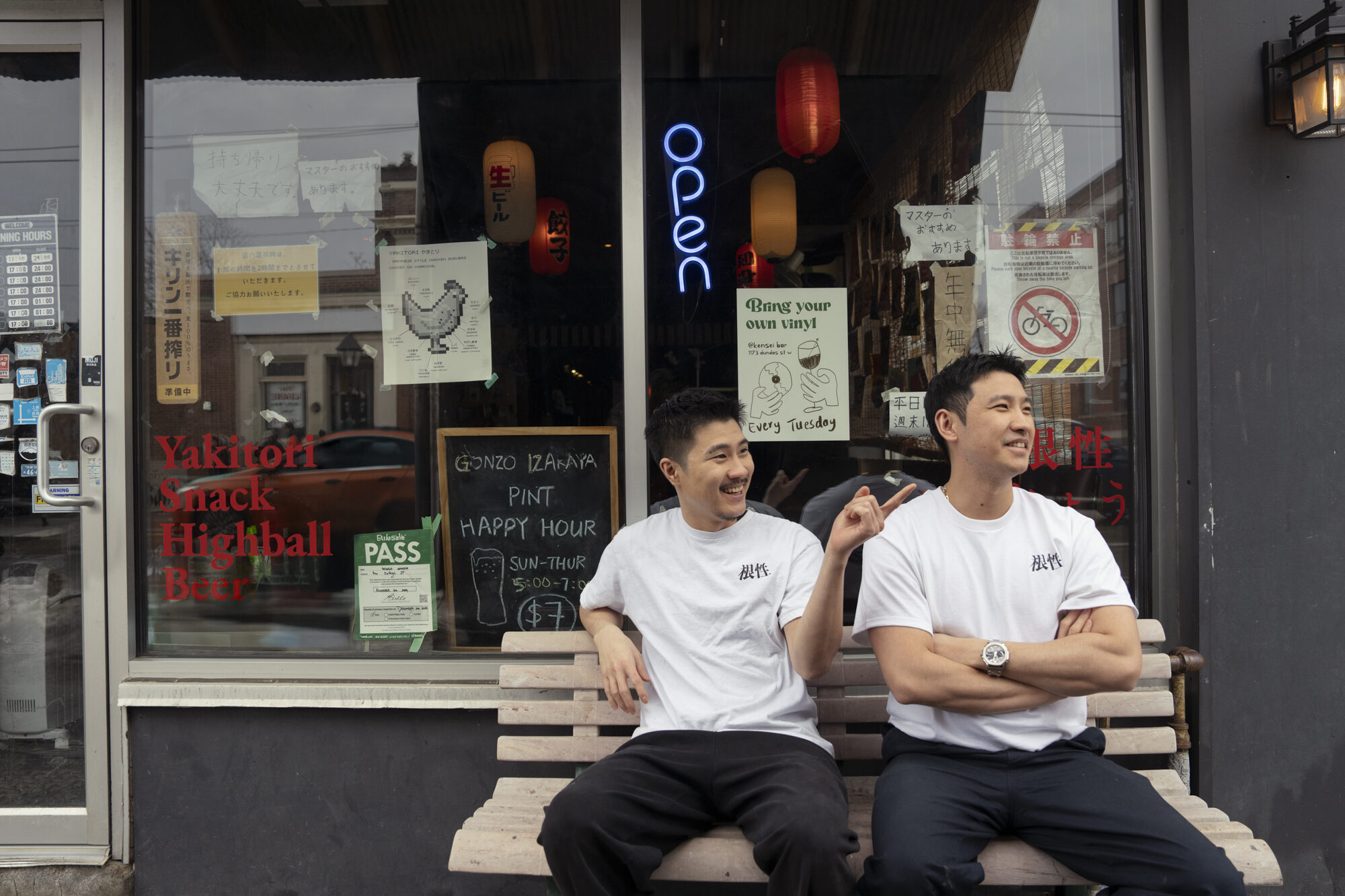 Two men seated outside restaurant storefront, casual documentary lifestyle photo