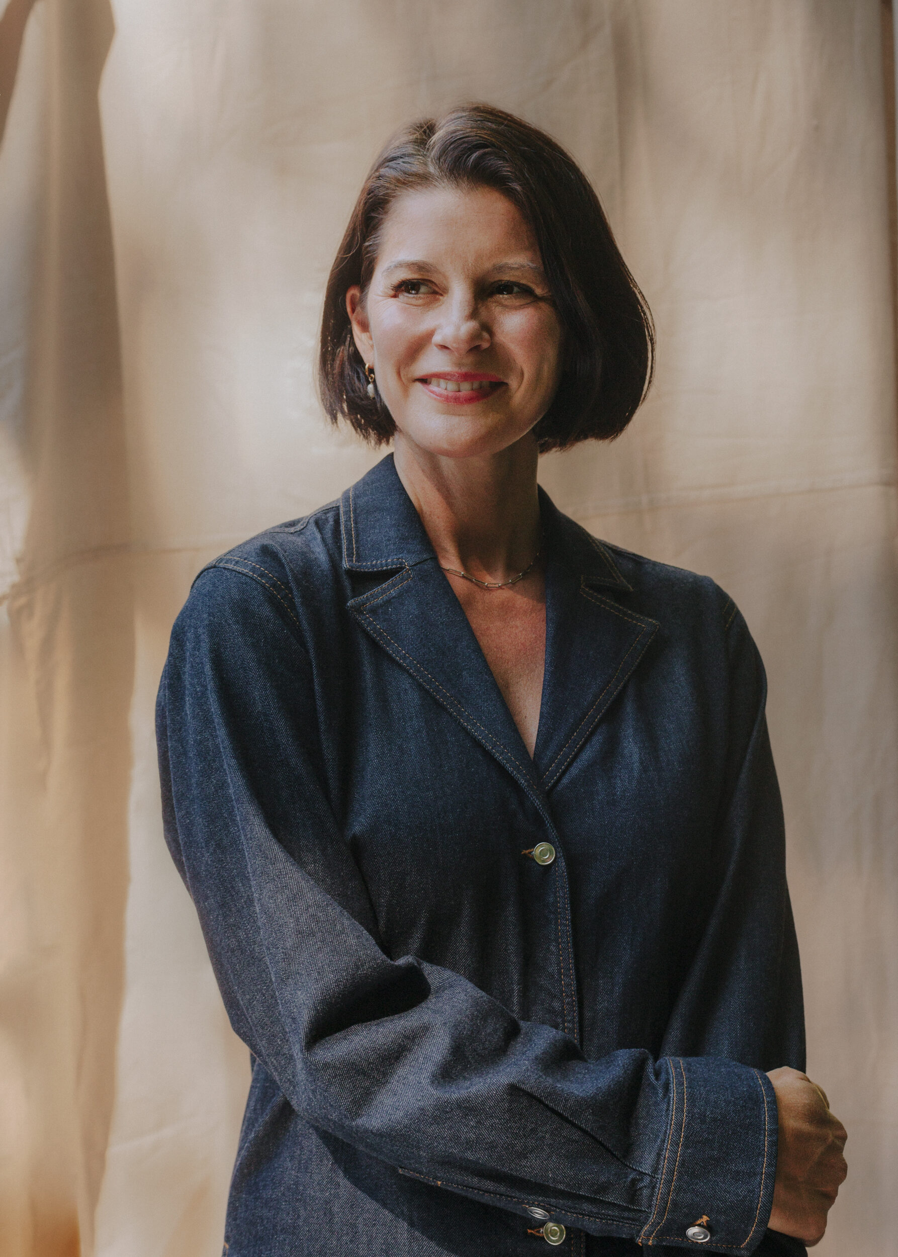 Portrait of a woman in a blue blazer against a warm neutral background, soft studio light.