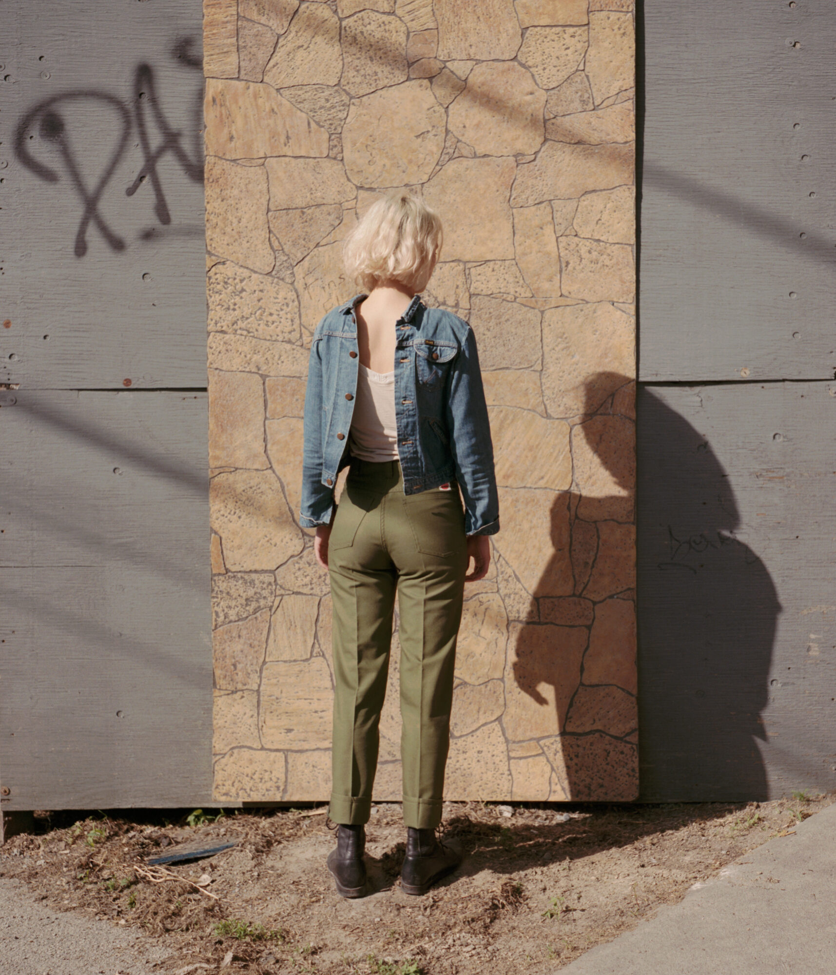 Person standing against a stone wall with long shadow in late-day light