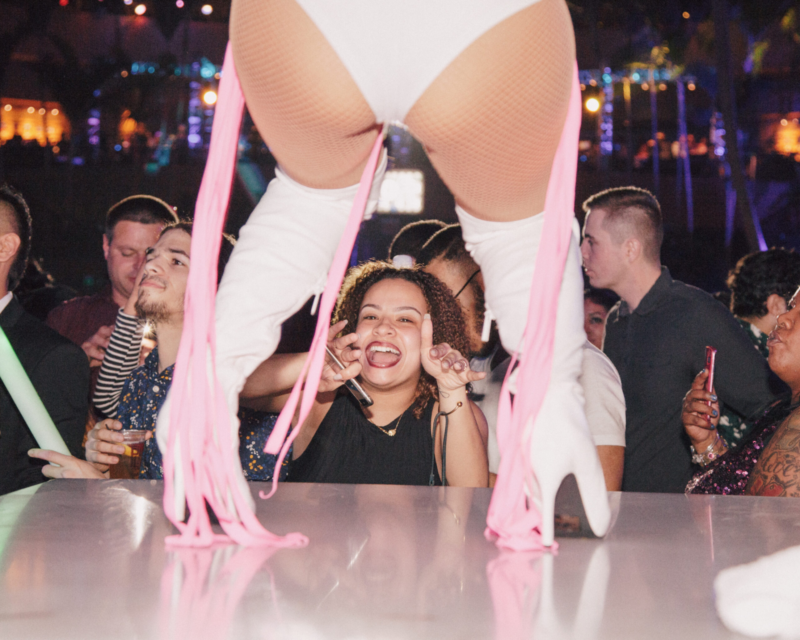 Nightlife scene with performer on stage and crowd watching, bright lights and high energy.