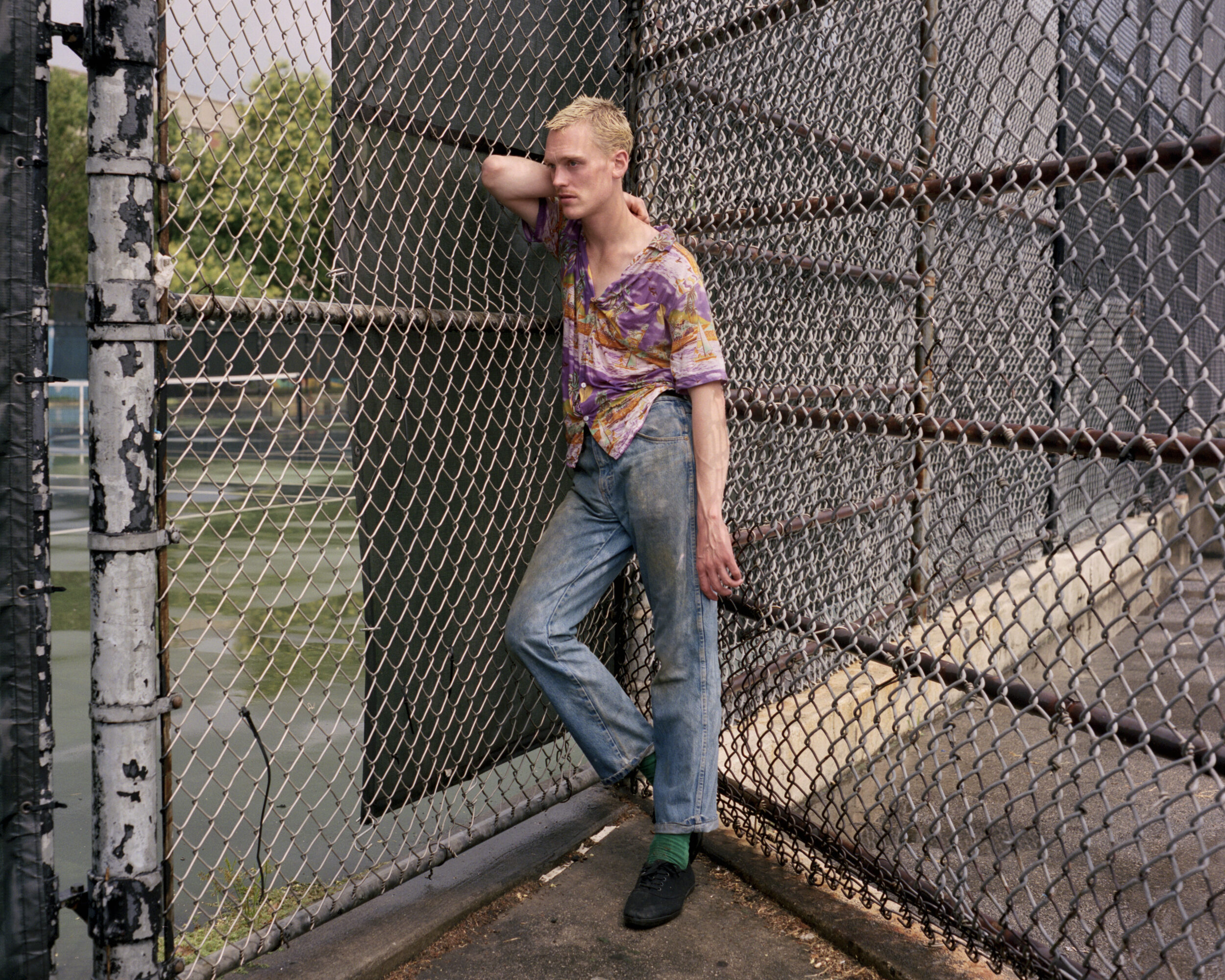 Person leaning against a chain-link fence in a sunlit outdoor corner