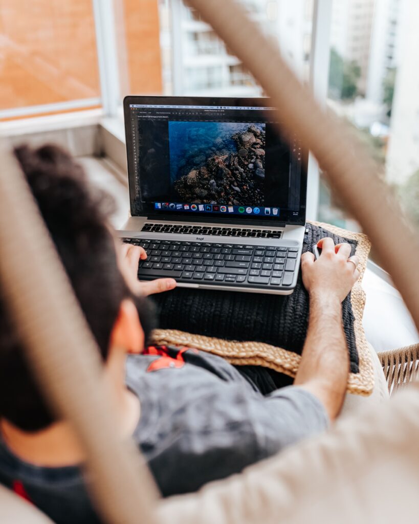 Person using a laptop and external keyboard while editing a photograph in Adobe Photoshop.